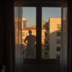 Dusky bedroom with heavy blackout curtains blurring outlines of interior and exterior, casting soft, uneven shadows and a faint human silhouette.