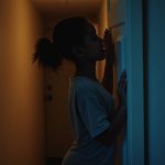 A parent quietly closes a child’s bedroom door under warm lamp light, capturing a peaceful moment near bedtime.
