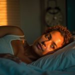 A middle-aged person lies awake on a neatly made bed at dusk, illuminated by soft window light and gazing thoughtfully at a wall clock, reflecting common feelings before a sleep clinic visit.